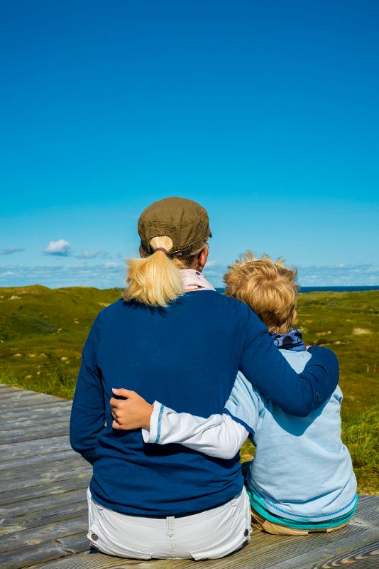 Mutter und Kind sitzen auf einem Holzweg und blicken auf eine grüne Landschaft im All Inclusive Familienurlaub in Deutschland 