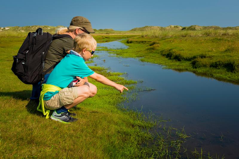 Mutter und Kind knien am Rand eines kleinen Wasserlaufs in All Inclusive Familienurlaub in Deutschland
