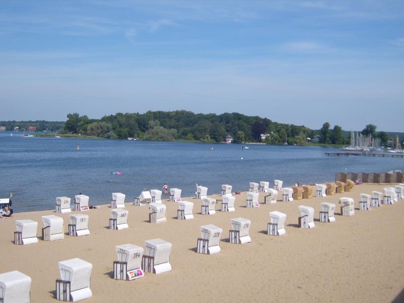Ausblick auf den Wannsee im Familien Kurzurlaub Berlin mit Strandkörben und dem Wasser mit Booten und einer Insel auf dem viele Bäume stehen
