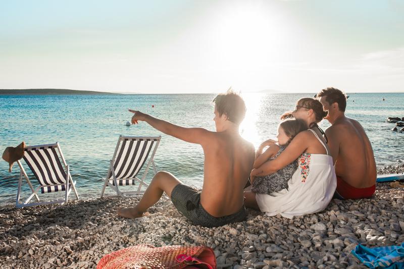 Eine Familien sitzt gemeinsam am Strand und schaut auf das Meer auf der Familienreise Kroatien