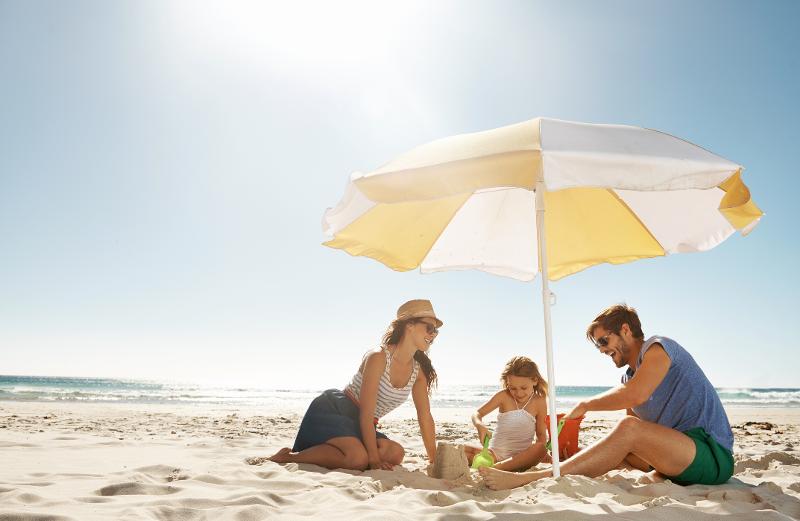 Mutter, Vater und ein Kind genießen die Sonne unter einem Sonnenschirm auf Familienreise