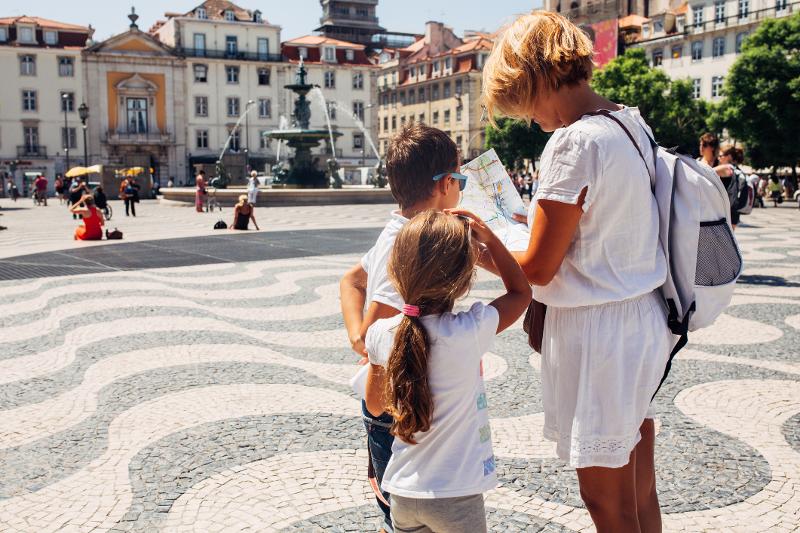 Mutter und Kinder stehen auf einem Platz in der Stadt auf der Familienreise Portugal. Das Wetter ist schön und sie schauen auf einen Stadtplan