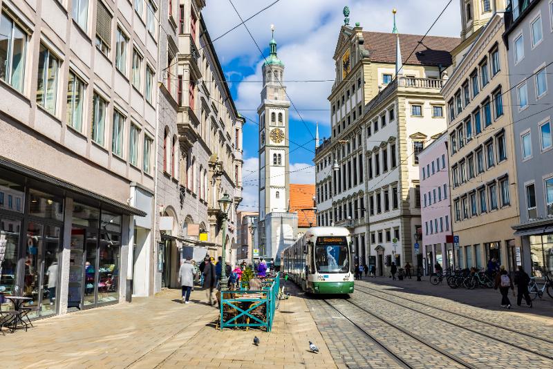 Eine Straße in Augsburg mit Straßenbahn und alten Häusern mit Kirche im Familienurlaub Bayern