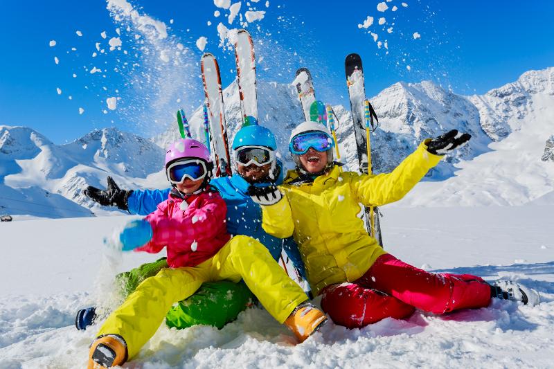 Drei Menschen in Skibekleidung, die im Familienurlaub in den Bergen Deutschland die Kamera lachen, im Hintergrund Schnee und Berge