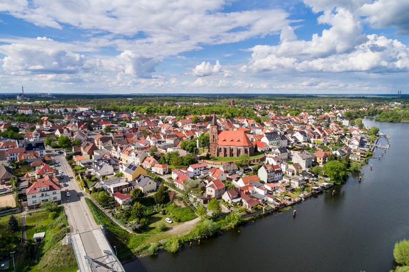 Eine Luftaufnahme eines charmanten Städtchens in Brandenburg mit roten Dächern und einem Fluss.