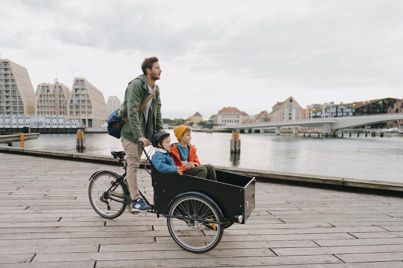 Ein Vater fährt Lastenrad und erkundigt mit seinen zwei Kindern gemeinsam im Familienurlaub Dänemark