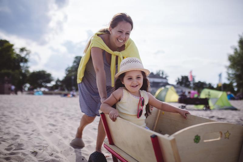 Mutter schiebt Tochter im Bollerwagen am Strand im Familienurlaub Deutschland