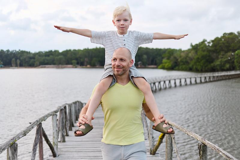 Vater trägt seinen Sohn auf den Schultern über einen Steg im Familienurlaub Deutschland