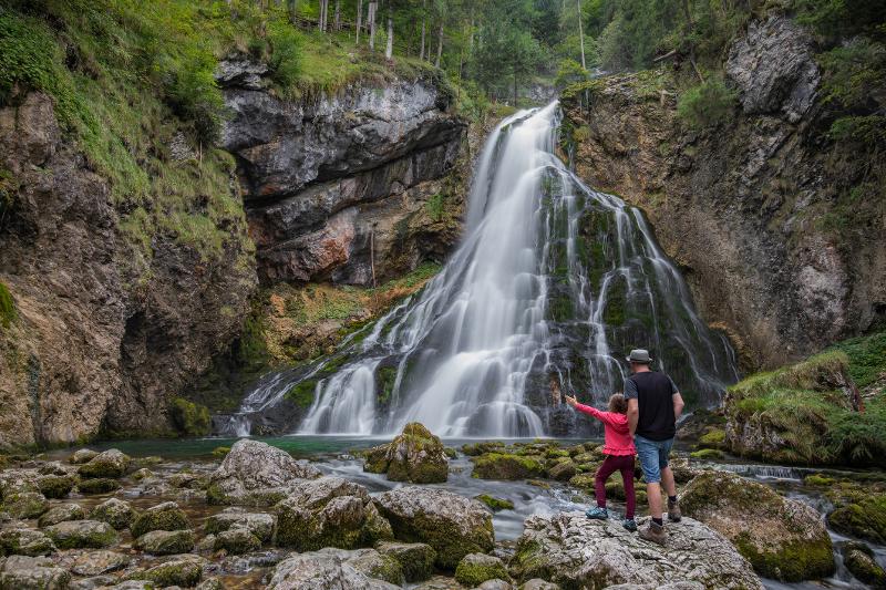 Vater und Tochter stehen im Familienurlaub Deutschland vor einer Bergkulisse mit  Wasserfall