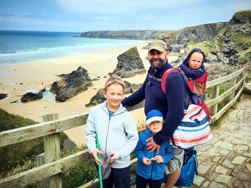Vater mit drei Kindern an einem malerischen Strand im Familienurlaub England