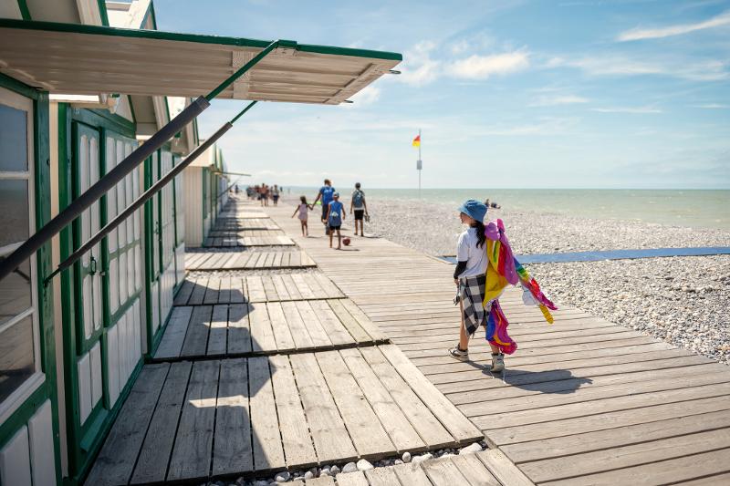  Familien laufen neben Strandhütten einen Steg entlang im Familienurlaub Frankreich Atlantikküste