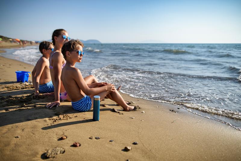  Geschwister sitzen am Strand und gucken aufs Meer im Familienurlaub Frankreich Côte d’Azur