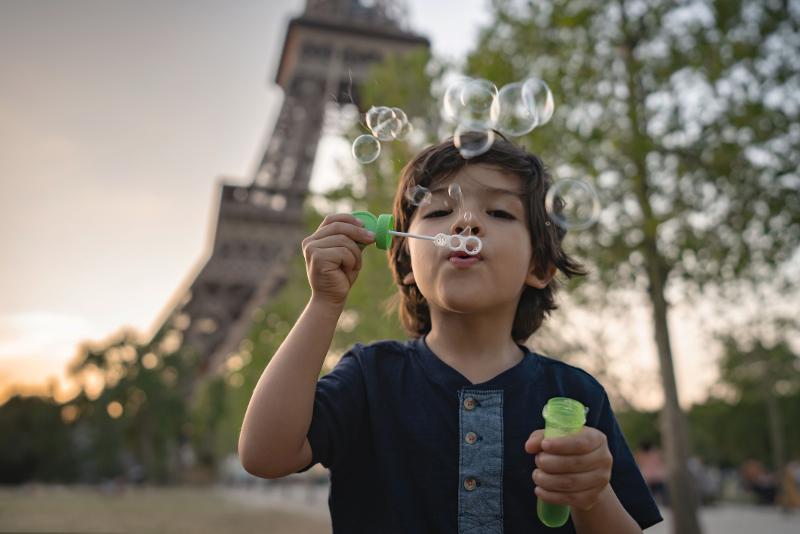  Ein Kind, das Seifenblasen in die Luft bläst, vor dem Hintergrund des Eiffelturms im Familienurlaub Frankreich