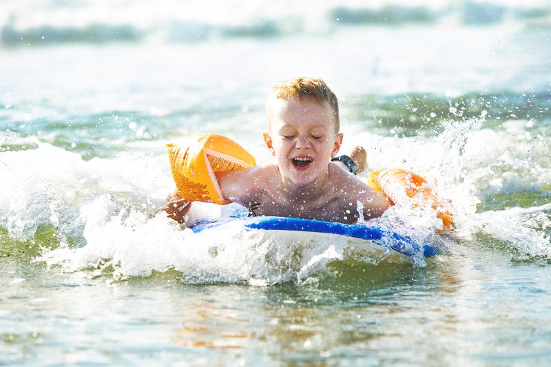 Ein Junge, der mit einem Surfbrett und Schwimmflügeln in den Wellen spielt