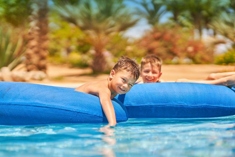 Zwei Kinder die im Familienurlaub Hurghada auf blauen Luftmatratzen im Pool liegen