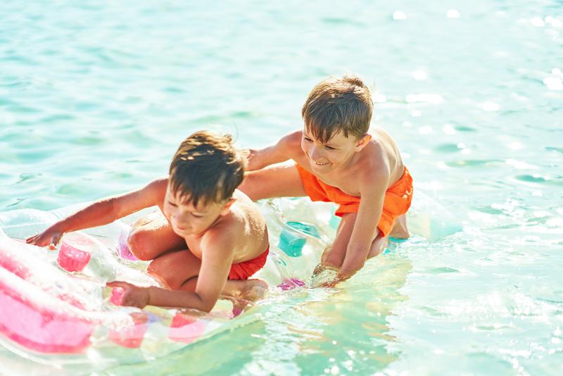 Zwei Kinder die auf einer Luftmatratze gemeinsam im Pool spielen im Familienurlaub Hurghada