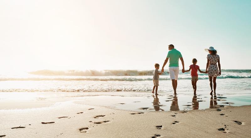  Familie spaziert Hand in Hand am Strand im Familienurlaub im Ausland