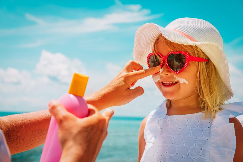 Ein Kind wird mit Sonnenschutz eingecremt, im Familienurlaub im Oktober am Meer