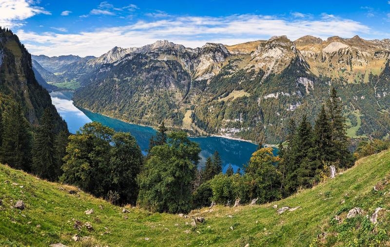 Aussicht auf einen See mit Bergen und grünen Wiesen auf denen Bäume stehen im Familienurlaub in den Bergen am See