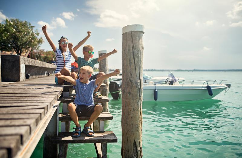  Kinder sitzen auf dem Steg am Wasser im Familienurlaub Italien All Inclusive