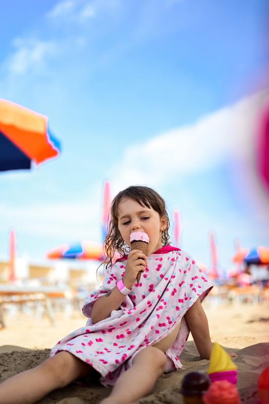  Ein Kind am Strand isst ein leckeres Eis im Familienurlaub Italien am Strand