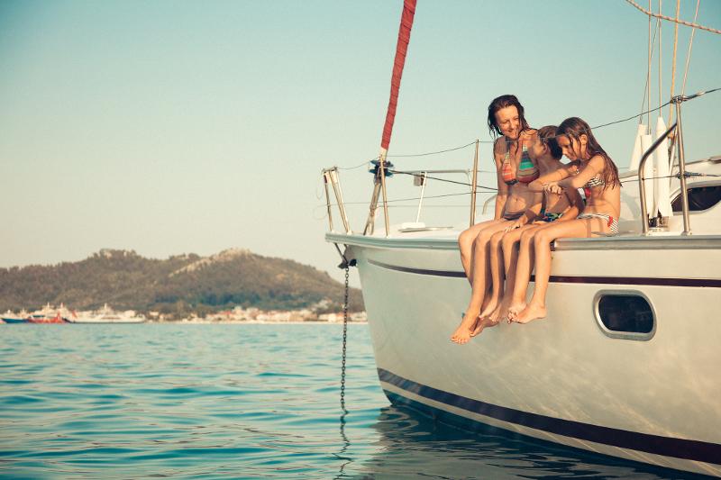 Ein Boot, auf dem eine Mutter und ihre Kinder im Familienurlaub Kroatien All Inclusive sitzen und auf das Meer schauen. Im Hintergrund weitere Boote und eine bergige Landschaft