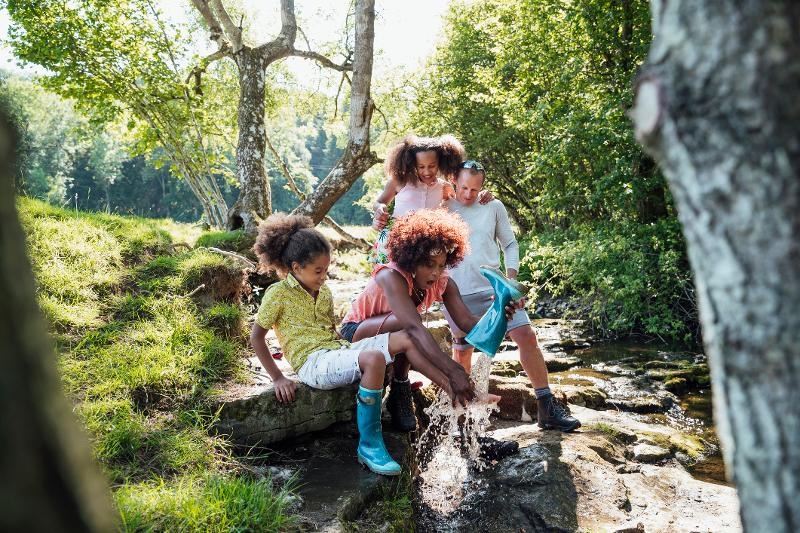 Eine Familie hat Spaß in der Natur und spielt mit Gummistiefeln im Wasser während ihres Familienurlaubs Last Minute