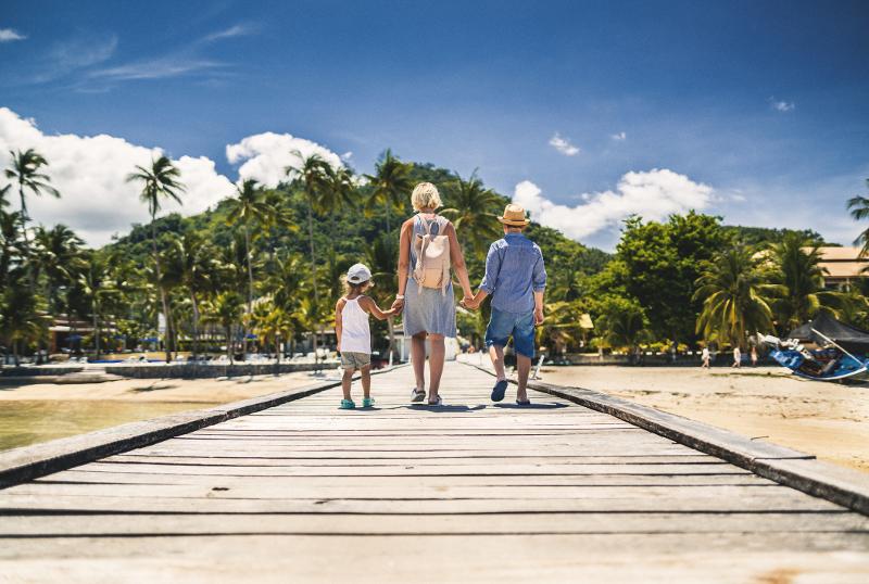 Eine Familie spaziert auf einem Steg an einem sonnigen Strand im Last Minute Familienurlaub