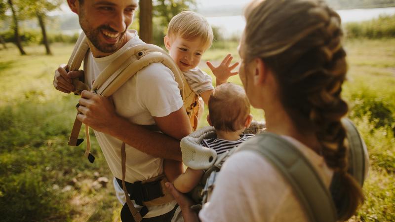 Eltern tragen ihre kleinen Kinder während eines Spaziergangs im Familienurlaub Last Minute