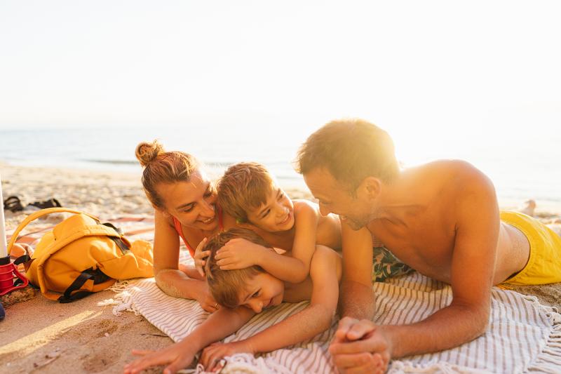 Familie liegt gemeinsam auf einer Decke am Strand