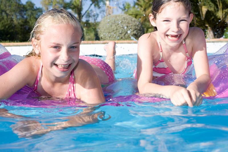 Zwei Mädchen treiben im Familienurlaub Mallorca Bungalow auf Luftmatratzen im Pool