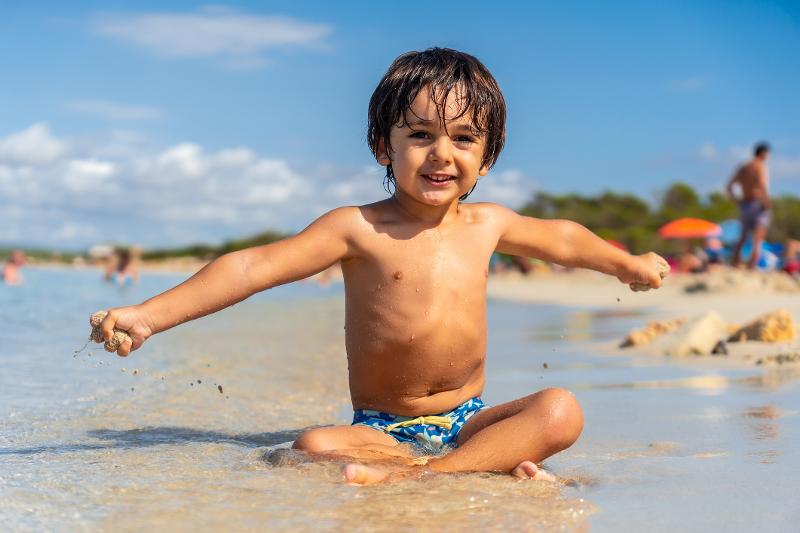 Ein Junge sitzt im flachen Wasser im Familienurlaub Mallorca Oktober am Strand