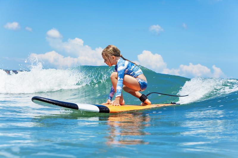 Ein Mädchen im Familienurlaub Mallorca auf einem Surfbrett 