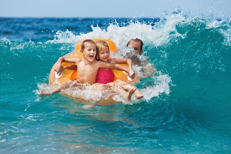 Ein Vater und zwei Kinder spielen im Familienurlaub Menorca All Inclusive in den Wellen