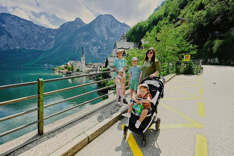 Eine Familie, die im Familienurlaub Österreich Sommer vor einem See steht, im Hintergrund eine Kirche und eine Berglandschaft