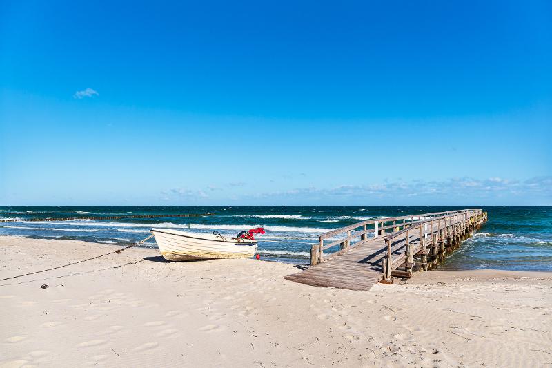Ein kleines altes Schifferboot steht neben einem Holzsteg am Strand im Familienurlaub Ostsee Last Minute 