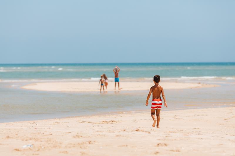 Kinder und Eltern in Badebekleidung, die im Familienurlaub Portugal All Inclusive auf Sandbänken am Meer stehen