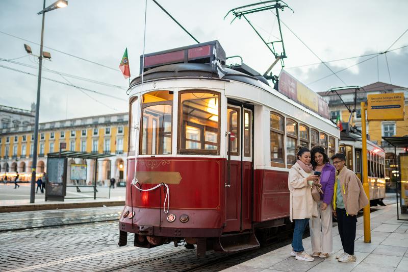 Drei Personen stehen vor einer traditionellen Straßenbahn im Familienurlaub Portugal