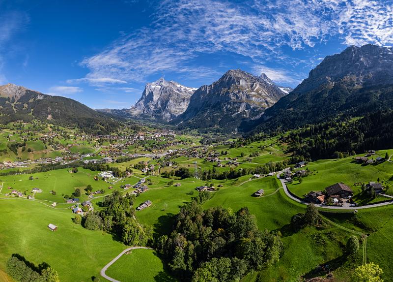 Blick auf eine grüne Berglandschaft in den Schweizer Alpen mit kleinen Dörfern und schneebedeckten Gipfeln