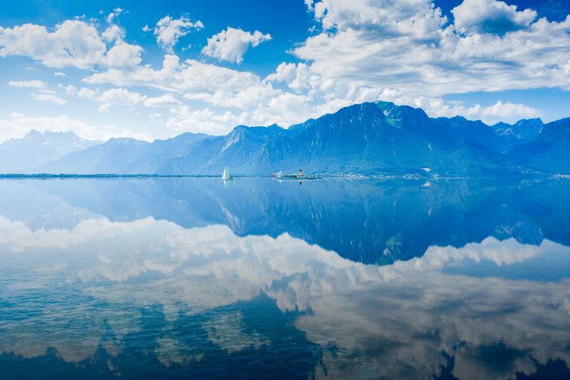 Ruhiger Genfersee mit spiegelnder Wasseroberfläche und umgebenden Bergen