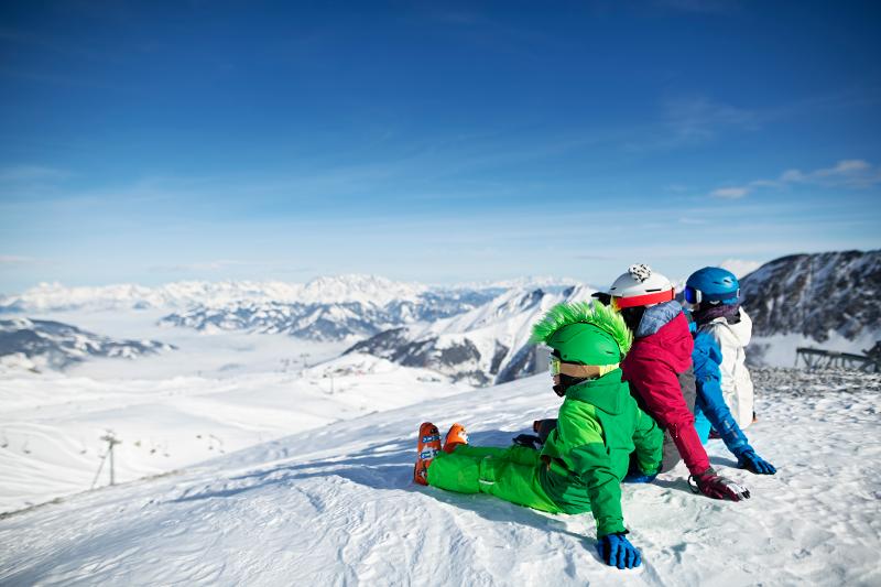 Drei Kinder sitzen im Familienurlaub im Schneeanzug auf einem Berg