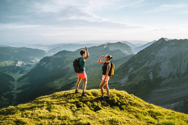 Zwei Personen stehen auf einem Berggipfel mit einer atemberaubenden Aussicht im Familienurlaub Sommer
