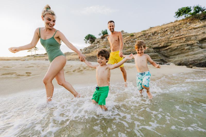 Eine Familie mit zwei kleinen Kindern, die im Familienurlaub Spanien All Inclusive in Badeklamotten am Strand entlang rennt