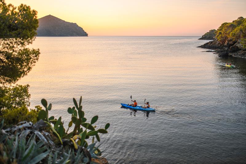 Ausblick auf das Meer mit Insel in der Dämmerung und auf dem Wasser fahren zwei Menschen in einem Kayak im Familienurlaub Spanien am Meer