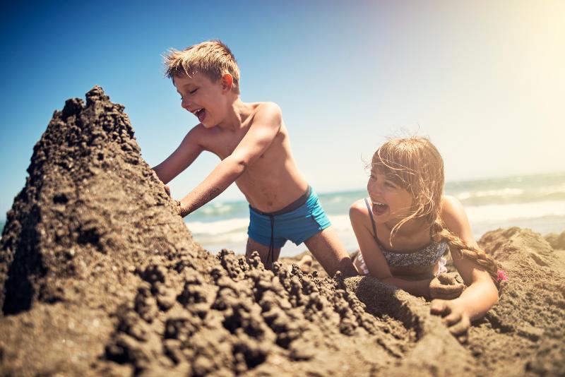 Zwei Kinder, die im Familienurlaub Spanien am Meer eine Sandburg bauen