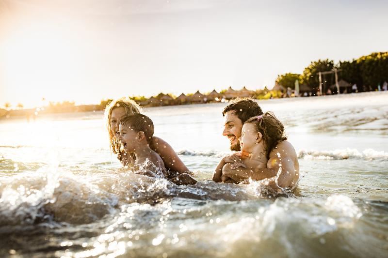 Eine Familie mit zwei Kindern, die im Familienurlaub Spanien am Meer im Wasser sitzt und badet