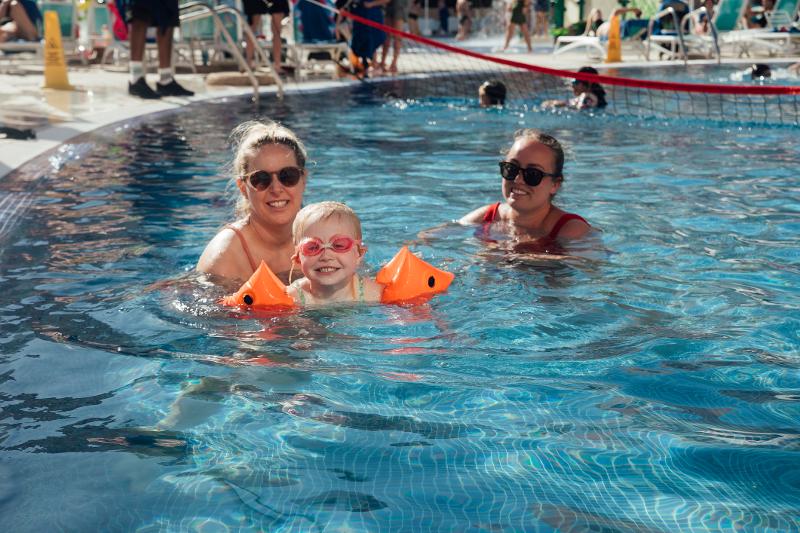 Zwei Erwachsene und ein glückliches Kind planschen vergnügt im funkelnden Wasser im Familienurlaub Spanien