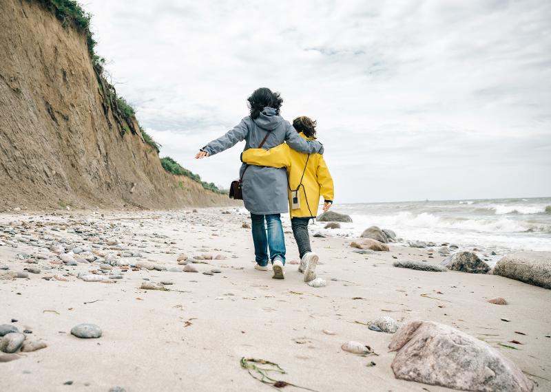 Zwei Personen laufen im Familienurlaub Arm in Arm am Strand entlang