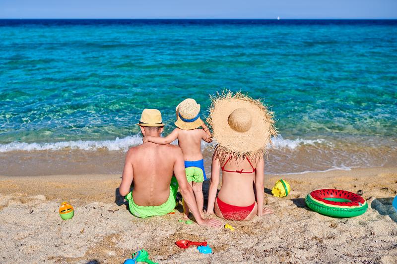 Eine Familie mit kleinem Kind, die im Familienurlaub Thessaloniki in Badesachen vom Strand aus auf das Meer gucken