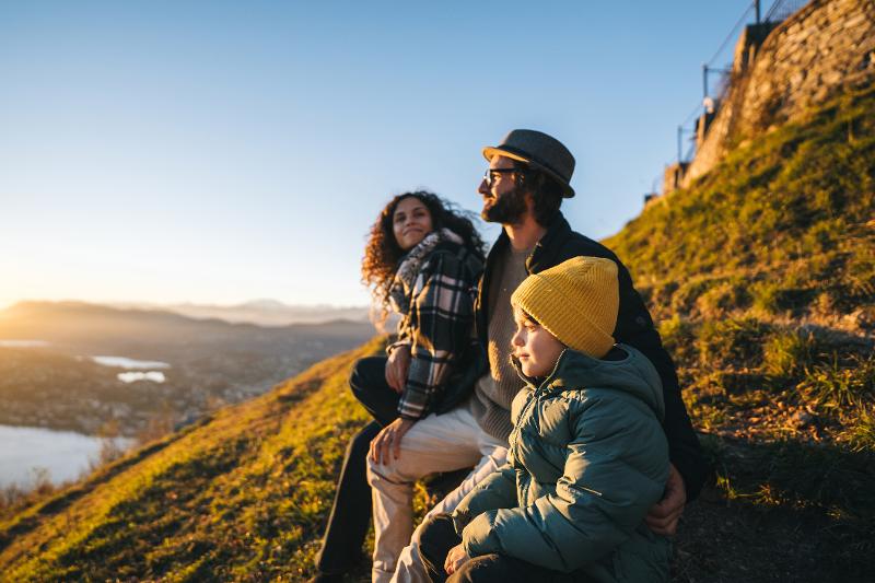 Drei Menschen sitzen im Familienurlaub auf einem Berg und genießen die Aussicht
